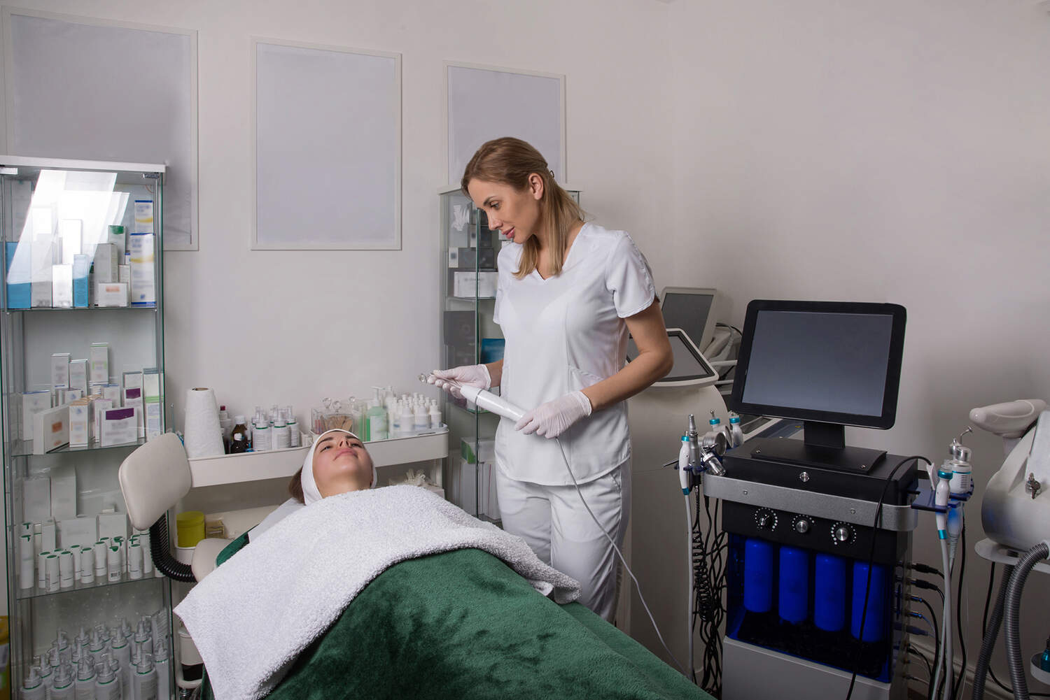 Cosmetologist is standing at laser hair removal machine and smiling. Woman in white coat, doctor of beauty salon waiting for start work with client.